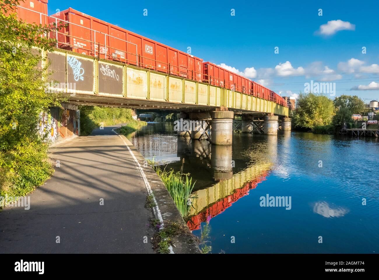 An orange goods train crossing on a green railway bridge over the RIver Nene in central Peterborough, Cambridgeshire, England Stock Photo