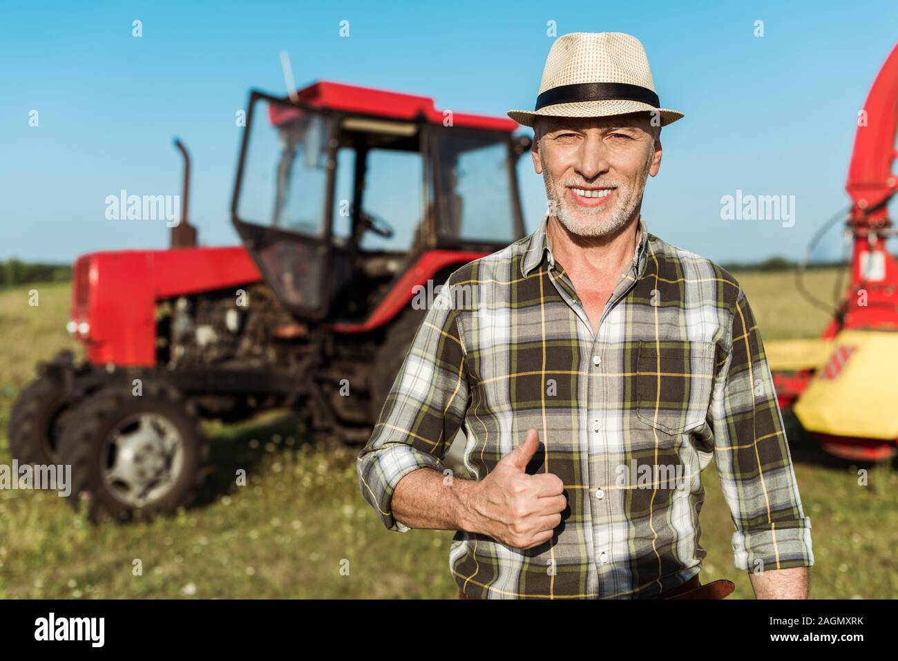happy farmer in straw hat showing thumb up near tractor Stock Photo - Alamy