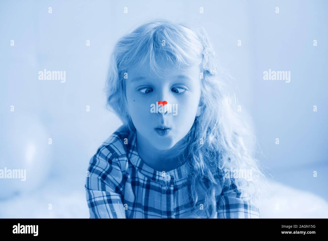Funny hilarious Caucasian cute adorable child girl looking at her nose with heart sticker on it. Cross-eyed kid squinting eyes. Valentine day holiday Stock Photo