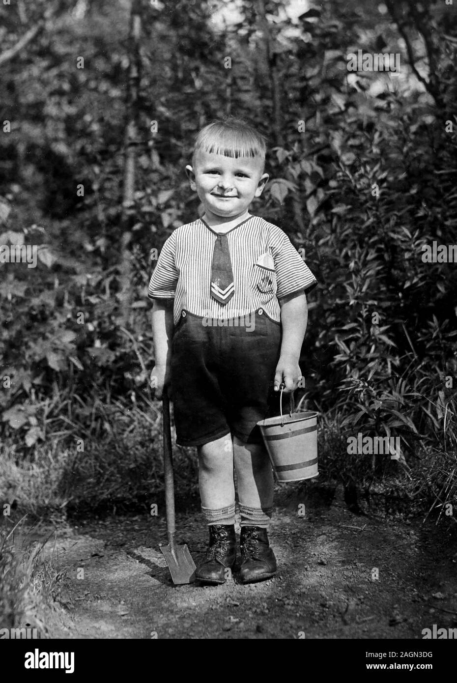 A young boy in a sailor suit poses with his sand bucket and shovel in Germany, ca. 1935. Stock Photo