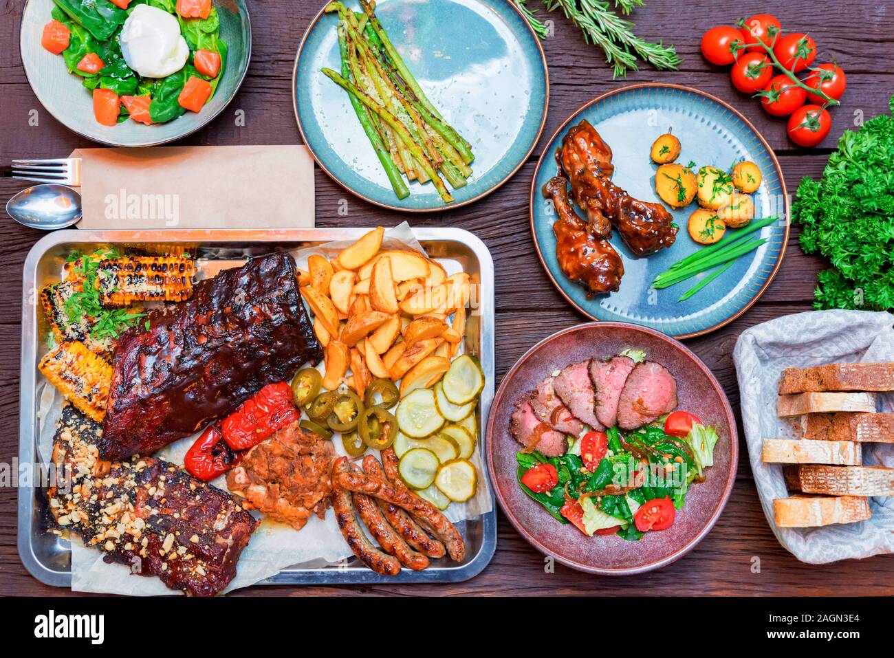 Top view of combo snack composition with grilled ribs, chicken, potato wedges, sausages, corn and jalapeno, salmon salad, asparagus, bread. Selective Stock Photo