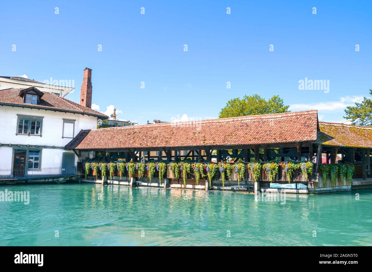 Old wooden bridge over turquoise Aare River in the Swiss city Thun. The bridge construction is decorated with traditional Alpine flowers. Tourist landmark in Switzerland. Historical center. Stock Photo