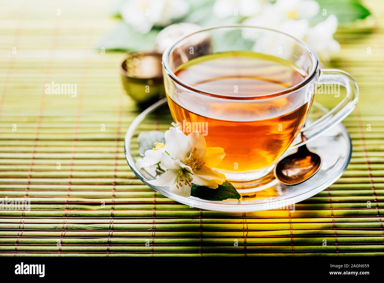 Glass of hot herbal tea on bamboo background closeup. Teacup with organic green tea and fresh jasmine flower on wooden table. Healthy alternative medi Stock Photo