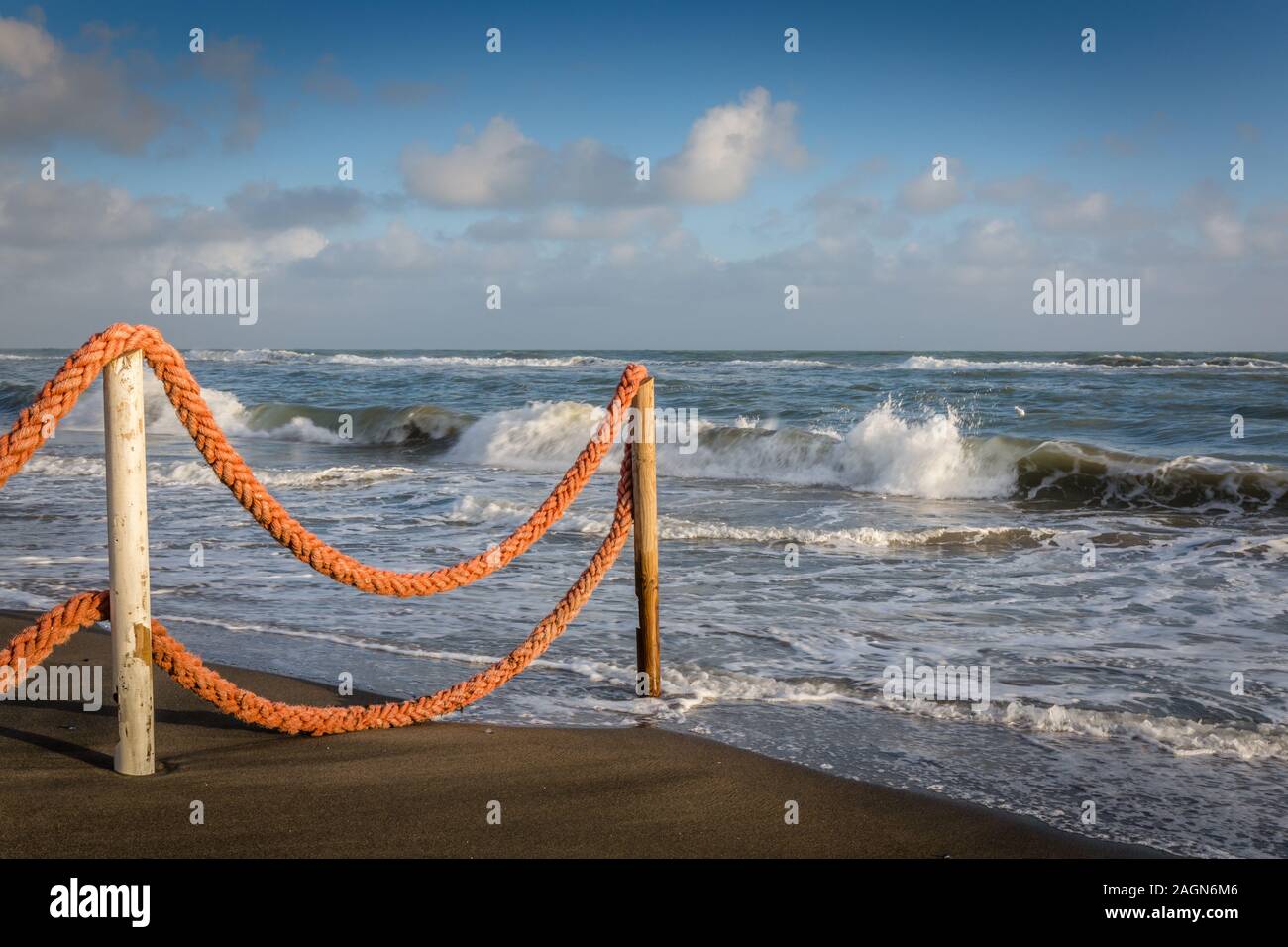 Late afternoon beach, sea edge with rope fence looking out to sea with crashing waves Stock Photo