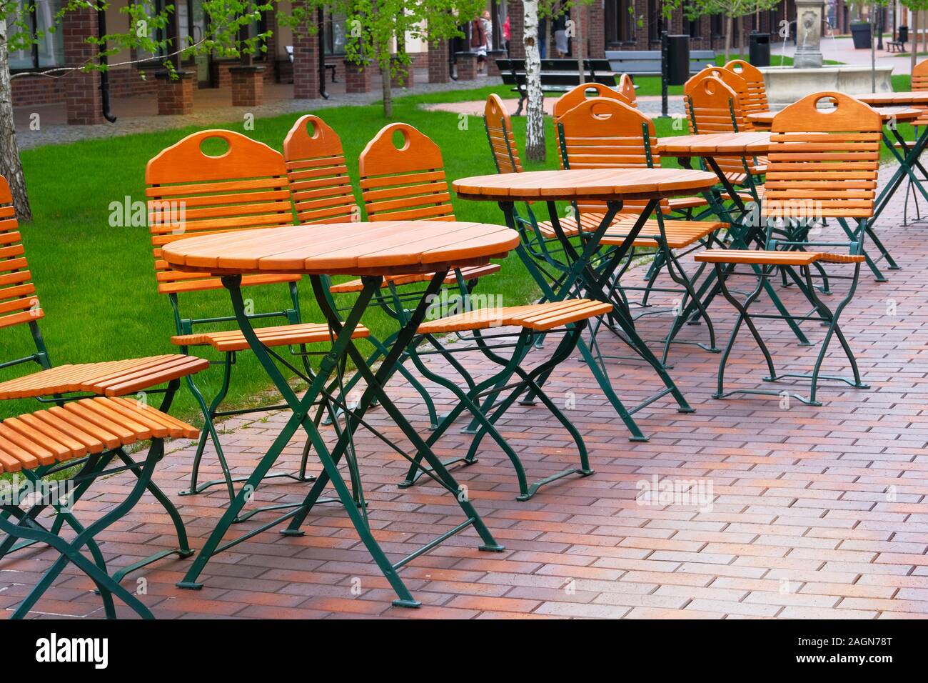 Chairs and tables in outdoor restaurant with wooden tops. Patio in garden in summer. Stock Photo