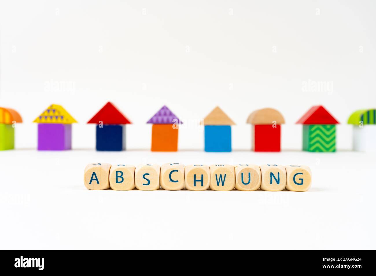 Wooden block with letters saying 'Abschwung' (German for recession) in front of colorful toy houses Stock Photo