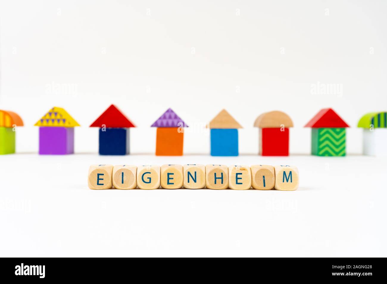Wooden block with letters saying 'Eigenheim' (German for buying homestead) in front of colorful toy houses Stock Photo