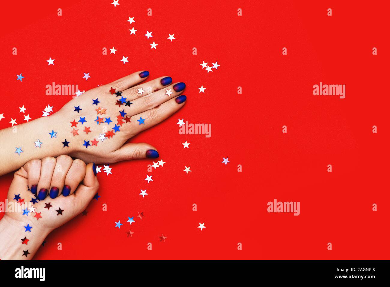Woman hands with blue manicure on red background with multicolor stars sprinkles. Holiday, party and Christmas concept. Stock Photo