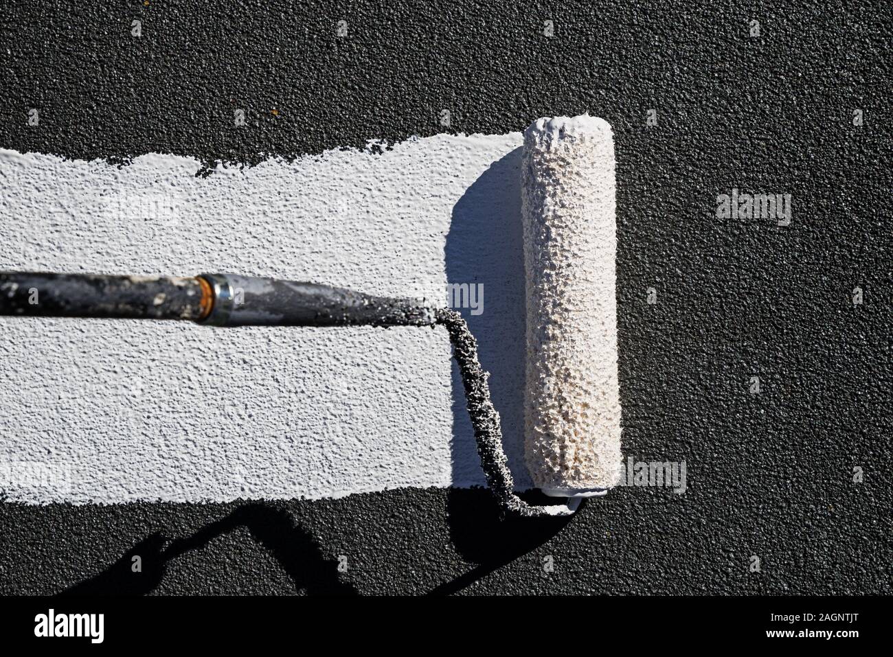 painting a roof with reflective white elastomeric coating with a paint roller Stock Photo