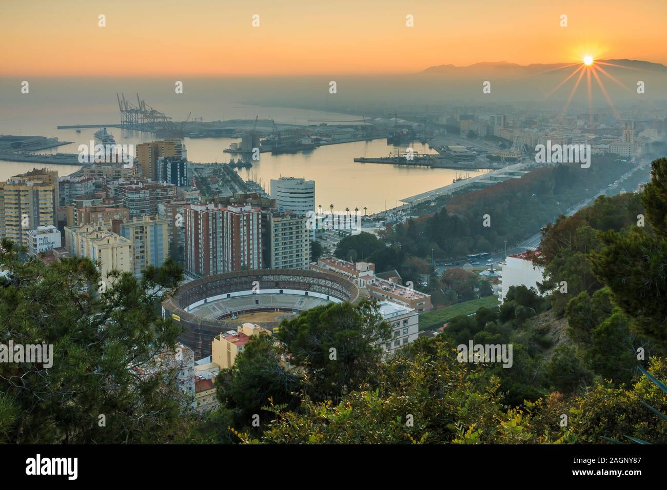 Sunset over Malaga on the Spanish Costa del Sol with a panoramic view of the city, the harbor, the houses, the trees, the bullring with street light Stock Photo