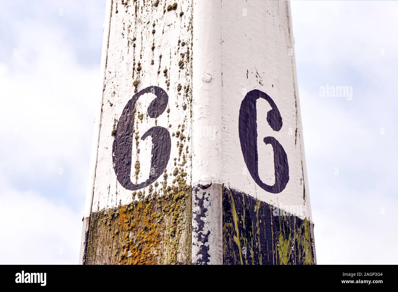 Horizontal image of an old weathered mooring post with number six painted on each side against a cloudy sky Stock Photo