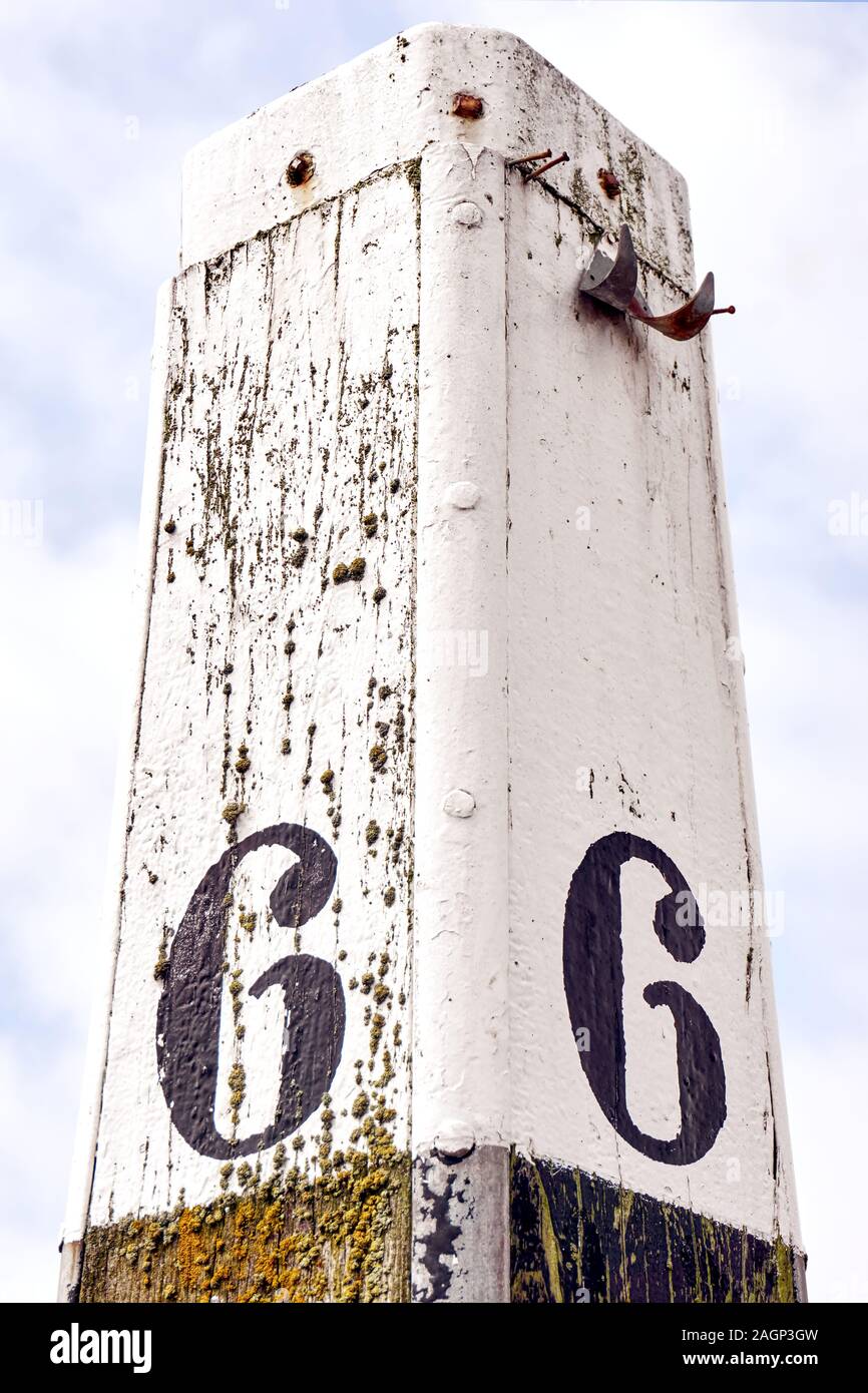 Vertical image of an old weathered mooring post with number six painted one each side against a cloudy sky Stock Photo