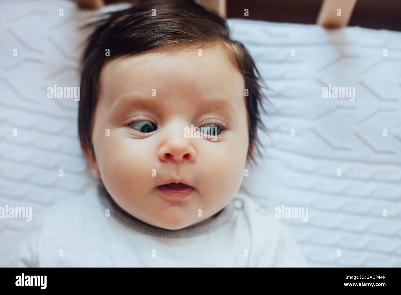 Surprised funny cute baby with blues eyes close portrait, lying in bed Stock Photo