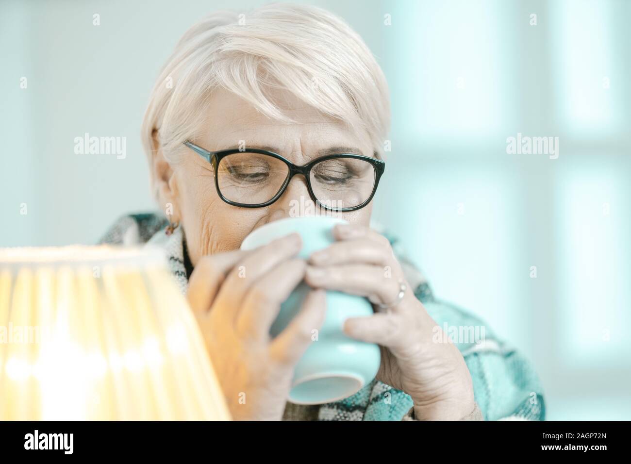 Granny Is Drinking Tea. She Enjoys Its Taste. Old Woman In Glasses Is