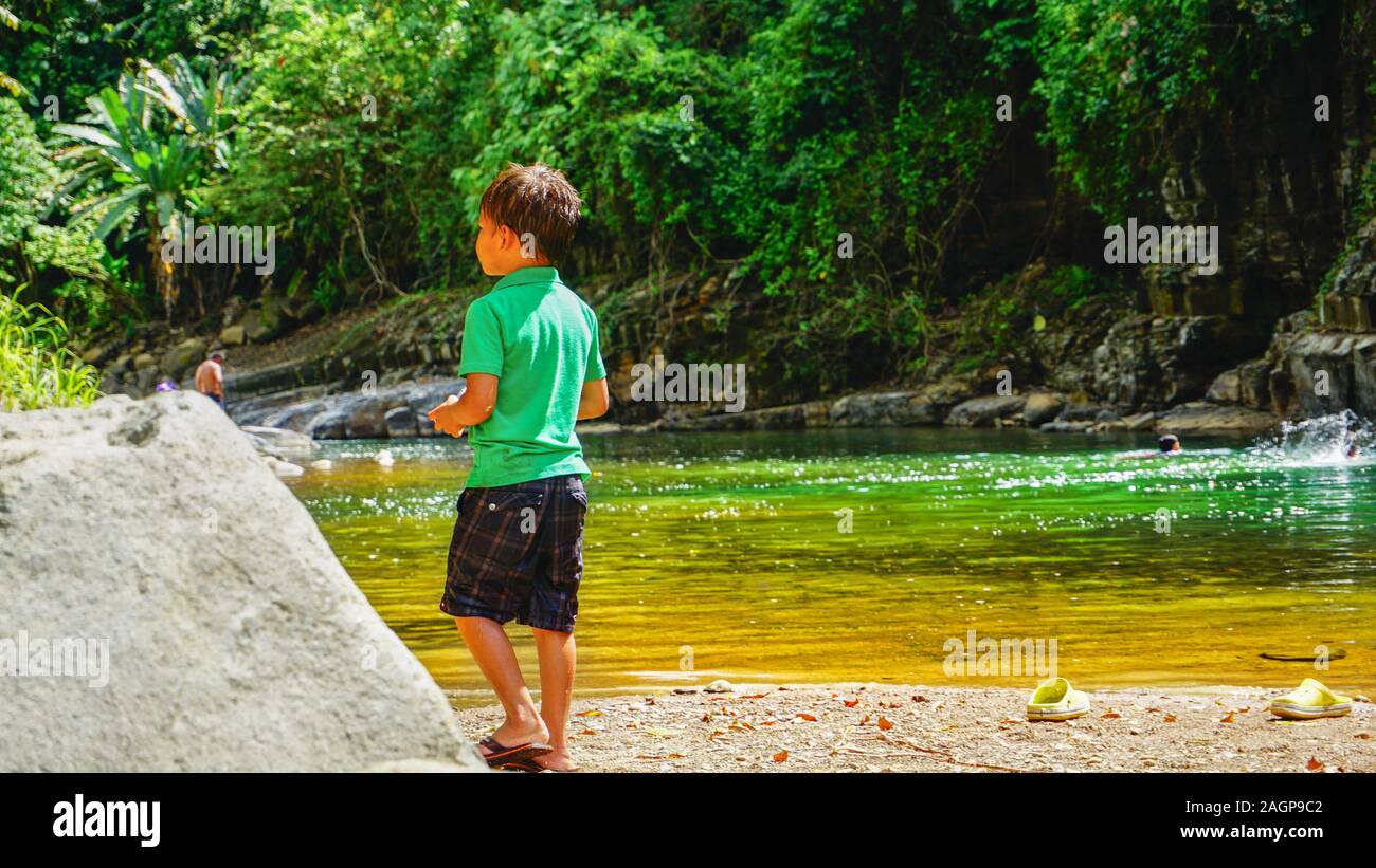 A small boy standing in the beautiful surrounding of Costa Rican wild green jungle environment and playing next to the natural swimming pool. Stock Photo