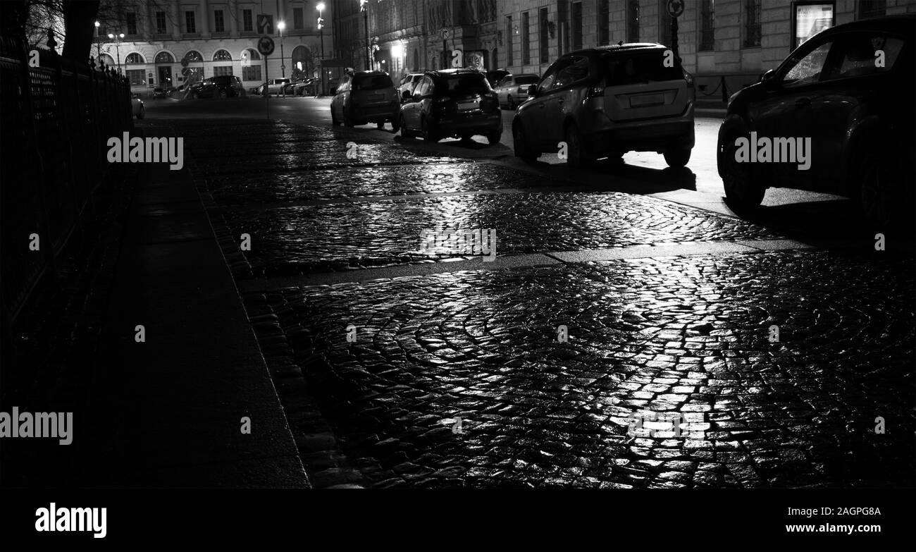 Rainy night in the city, wet shiny cobblestone pavement with parked cars Stock Photo