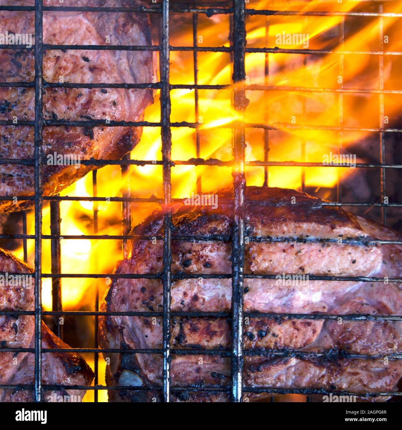 Few pieces of slightly burnt meat on charred grate with fire and smoke