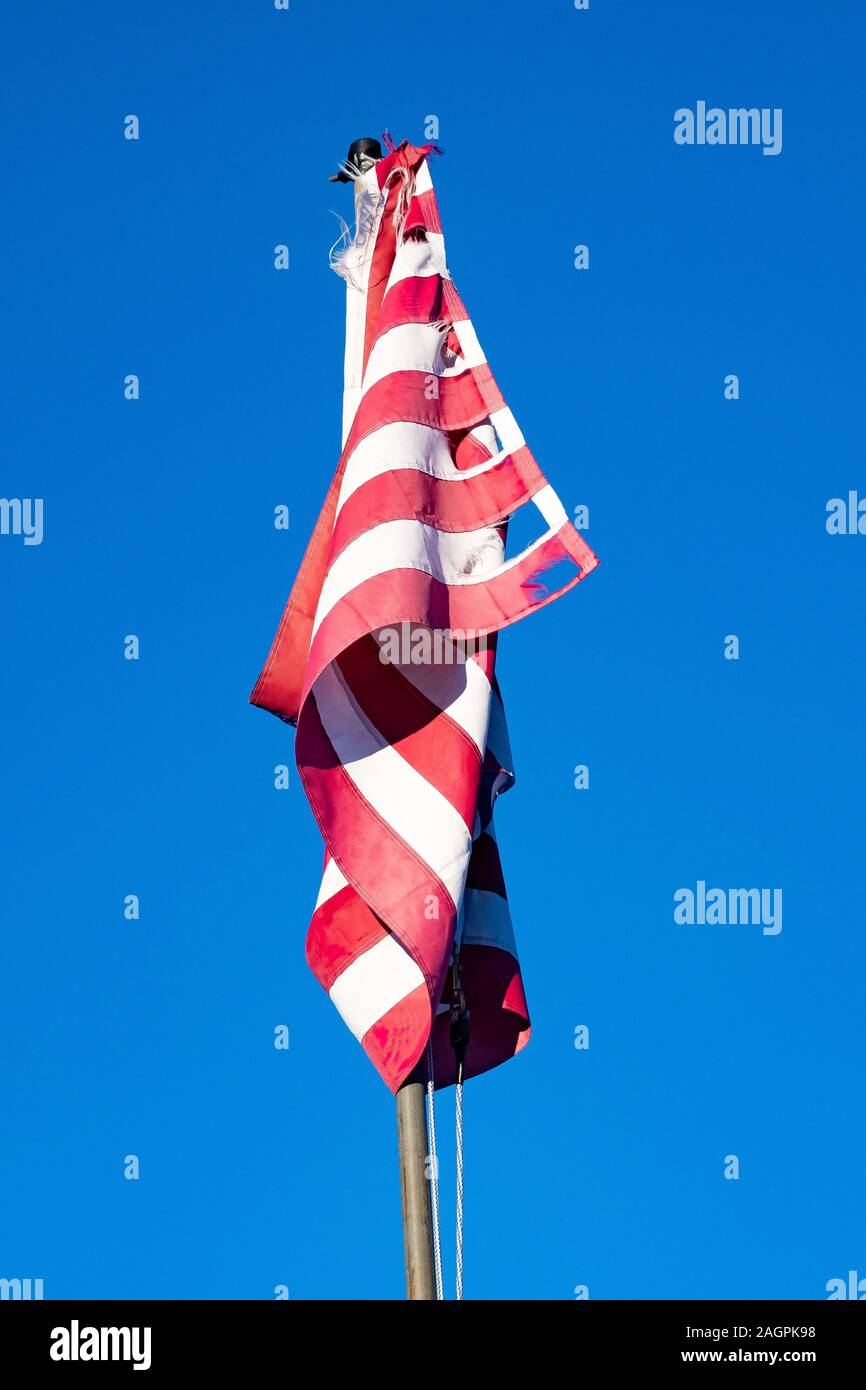 A twisted torn neglected American Flag against a clear blue sky in Speculator, NY USA Stock Photo