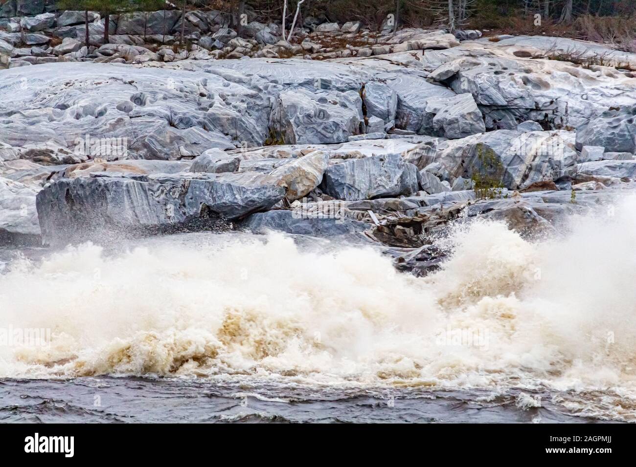 Water rushes into a river just below a hydroelectric dam. The whitewater crashes into the surface of the waterway creating mist and large white rapids Stock Photo