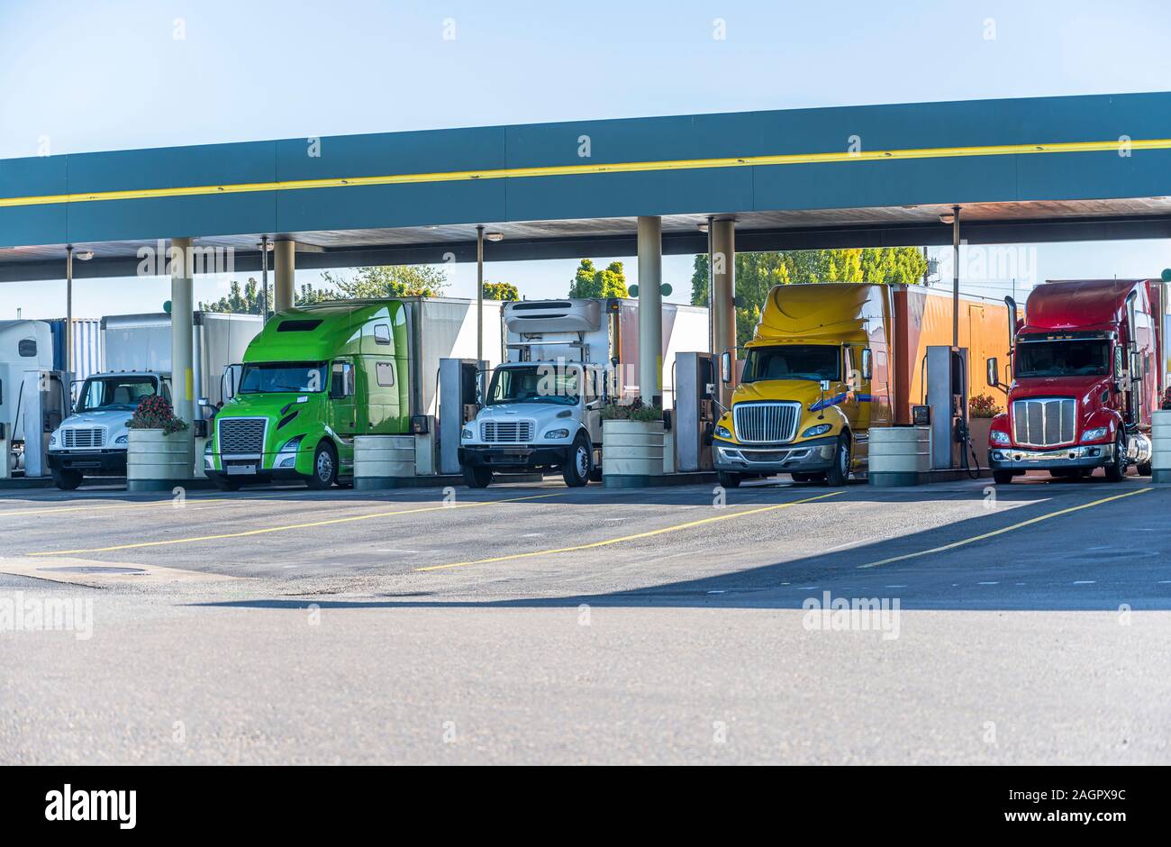 Different big rigs long and local haul semi trucks standing  under the eaves on the truck stop fuel station for refueling and continuation of the carg Stock Photo