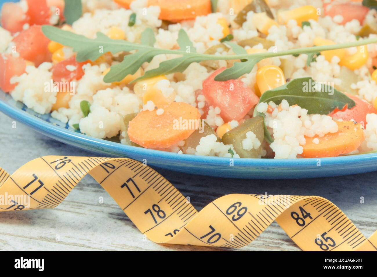 Tape measure and fresh salad with vegetables and couscous groats. Light