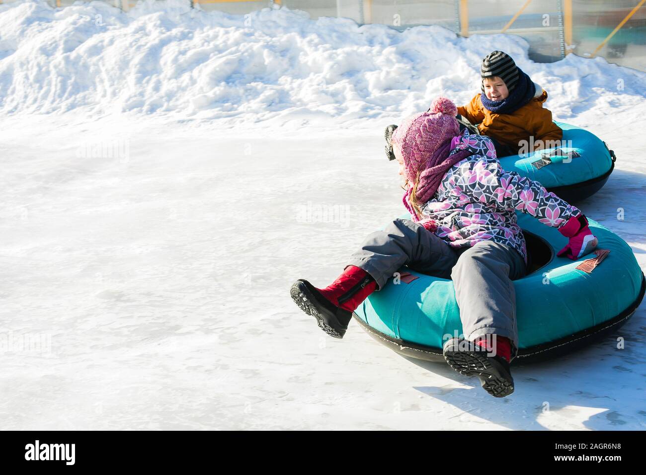 Little kids roll down the ice slide on tubing. Wintertime. Fun and games, outdoor activities concept. Stock Photo