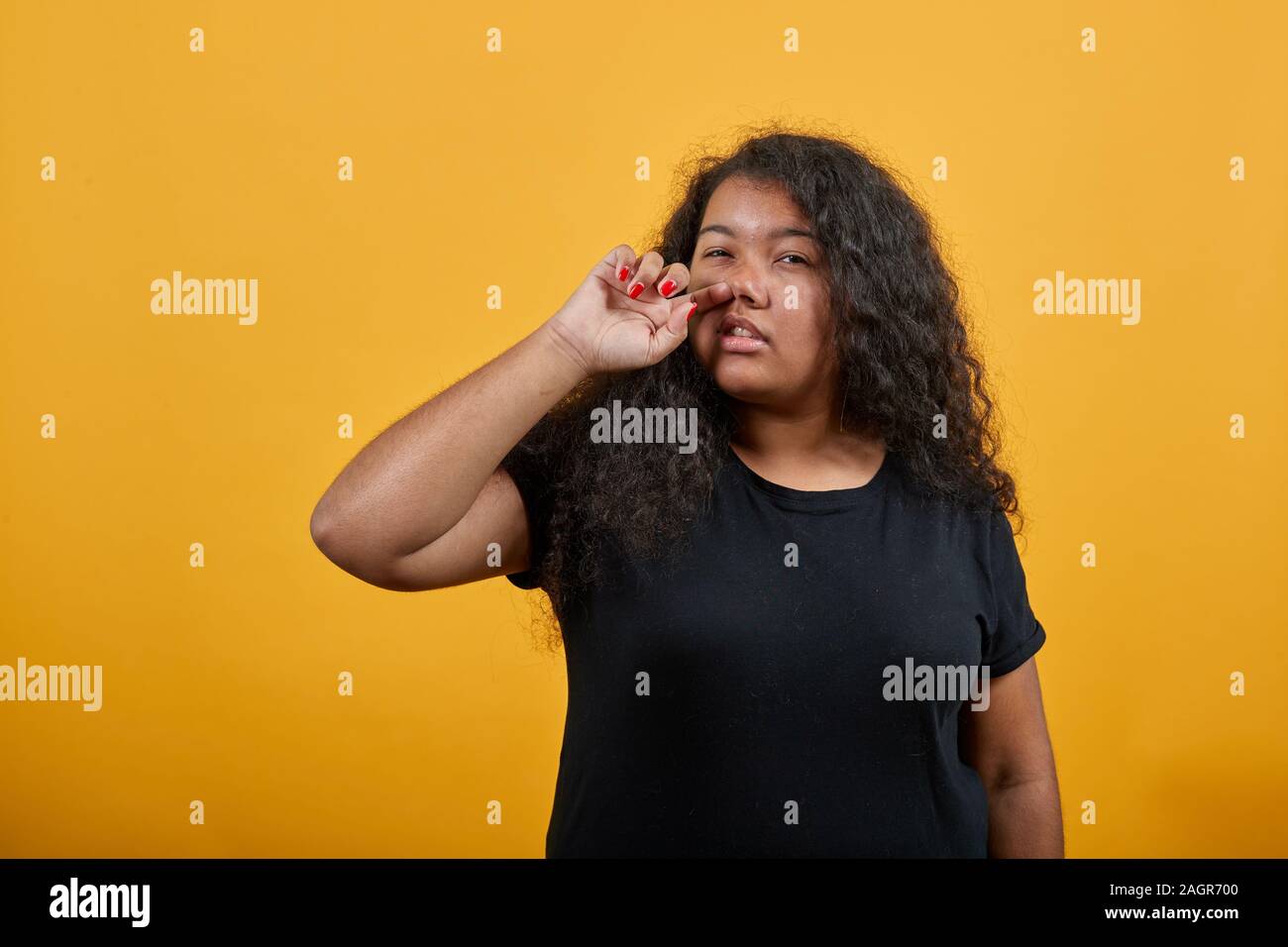 Afro-american young woman with overweight picking nose, looking at camera Stock Photo