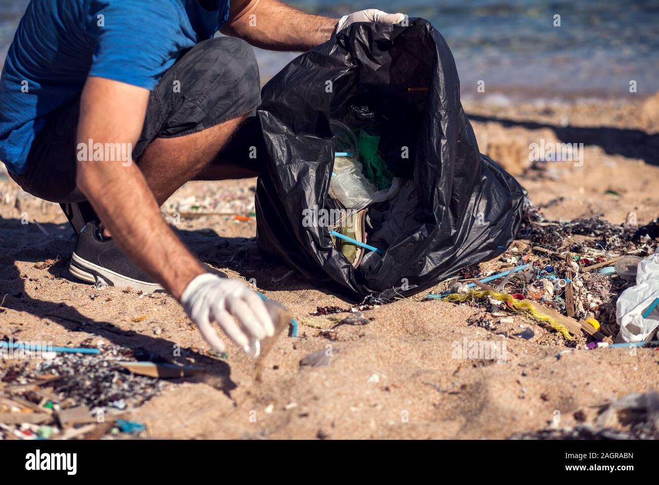 Man volunteer with black bag collect garbage on the beach. Environmental pollution concept Stock Photo