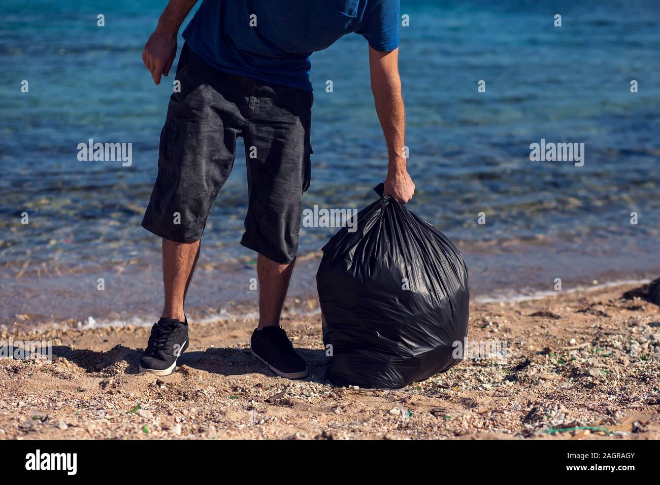 Man volunteer with black bag collect garbage on the beach. Environmental pollution concept Stock Photo