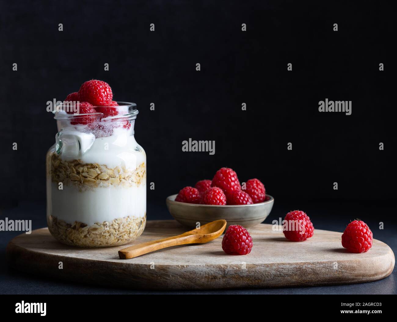 healthy vegan breakfast of yoghurt with muesli and raspberry on a dark background with copy space Stock Photo