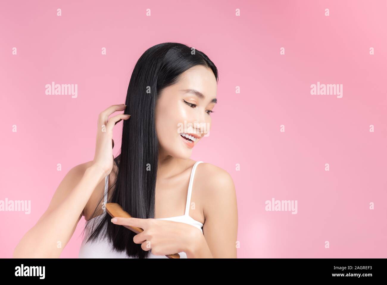 Beautiful young Asian woman holding her healthy hair and combing her hair on pink background. Stock Photo