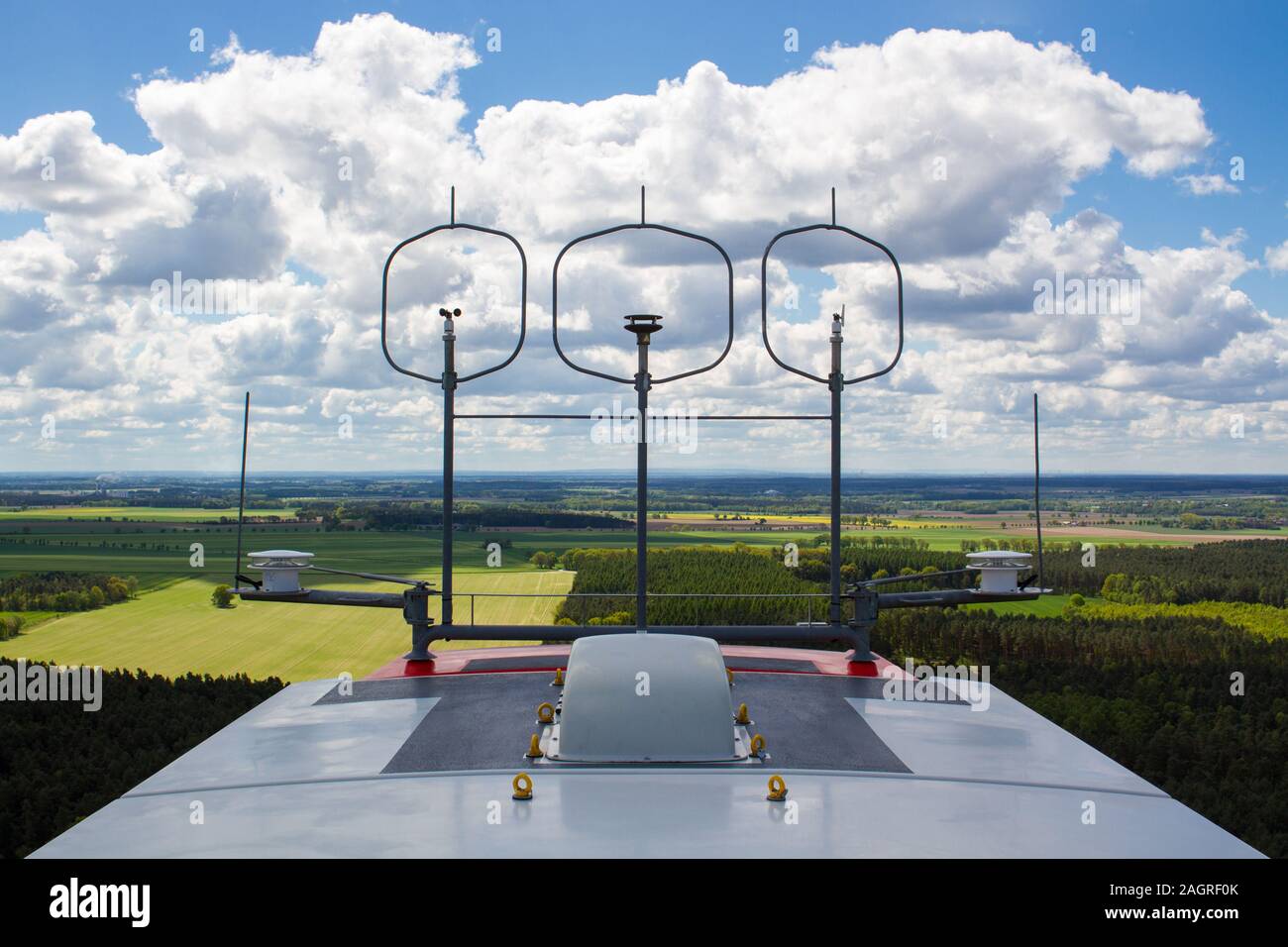 Measurement devices (cup anemometer, ultrasonic anemometer, wind vane) and aviation lights on the nacelle roof of a wind turbine with fields and cloud Stock Photo