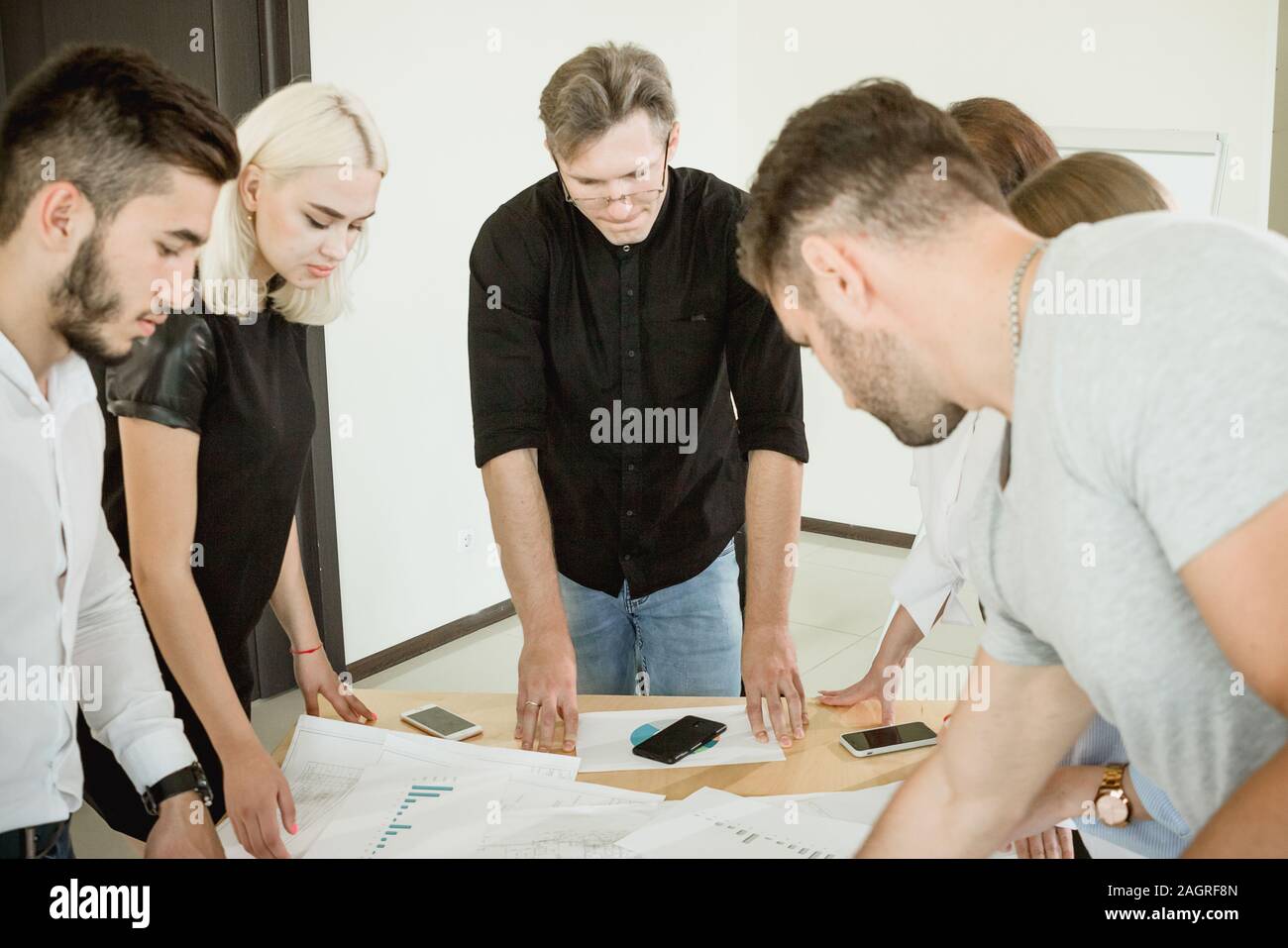 Hard work on the project. All employees and the project manager are standing above the table with documents discussing the project. Stock Photo