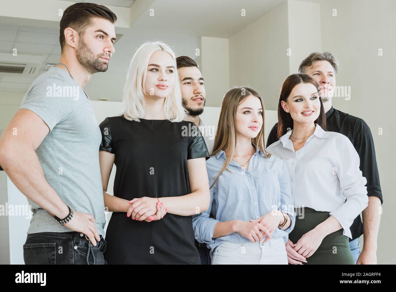 A group of young cheerful people are looking forward and up They are located in an office spacious light room Stock Photo