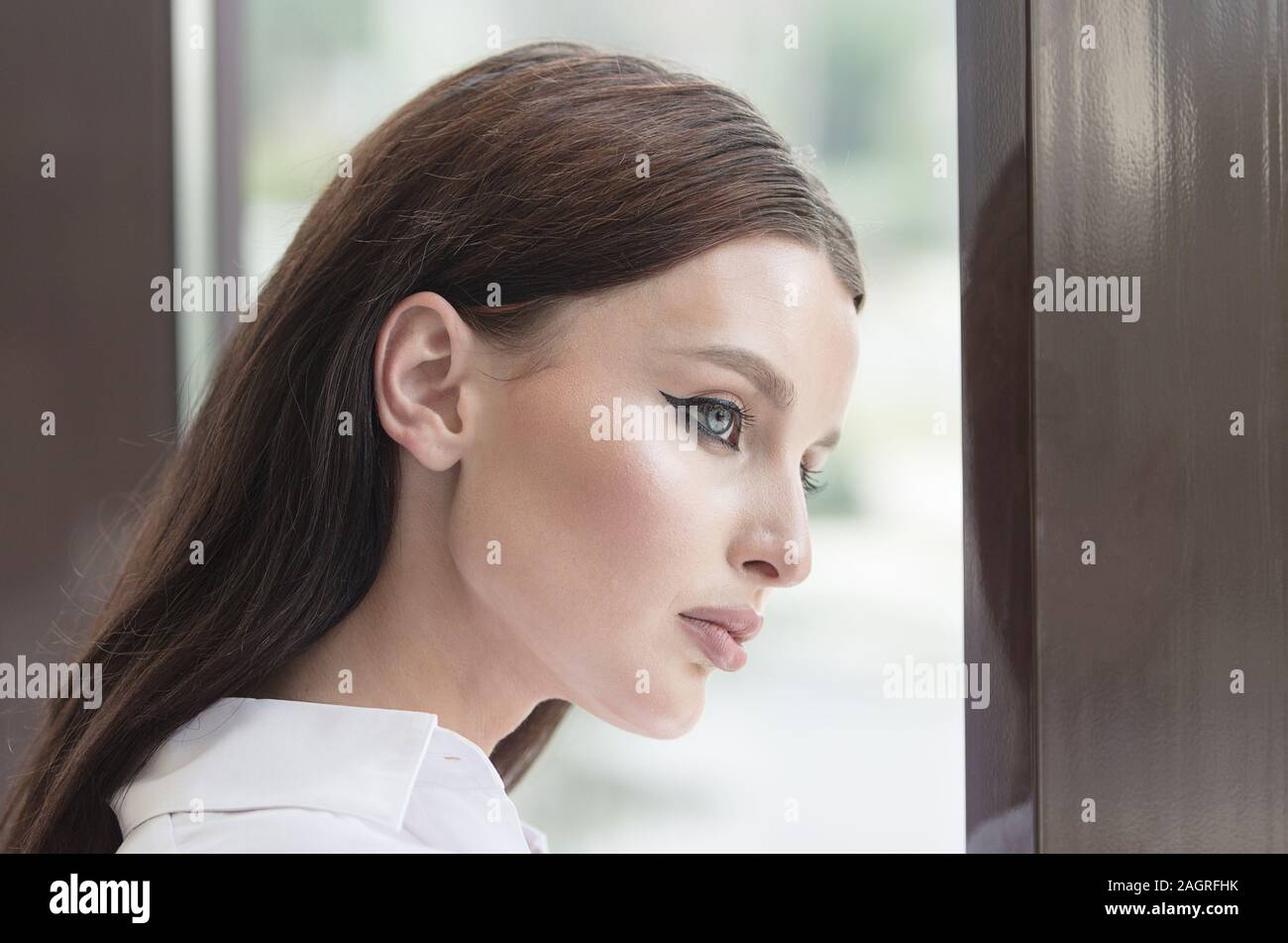 Bored business lady with beautiful blue eyes is leaning by office window looking to the street Stock Photo