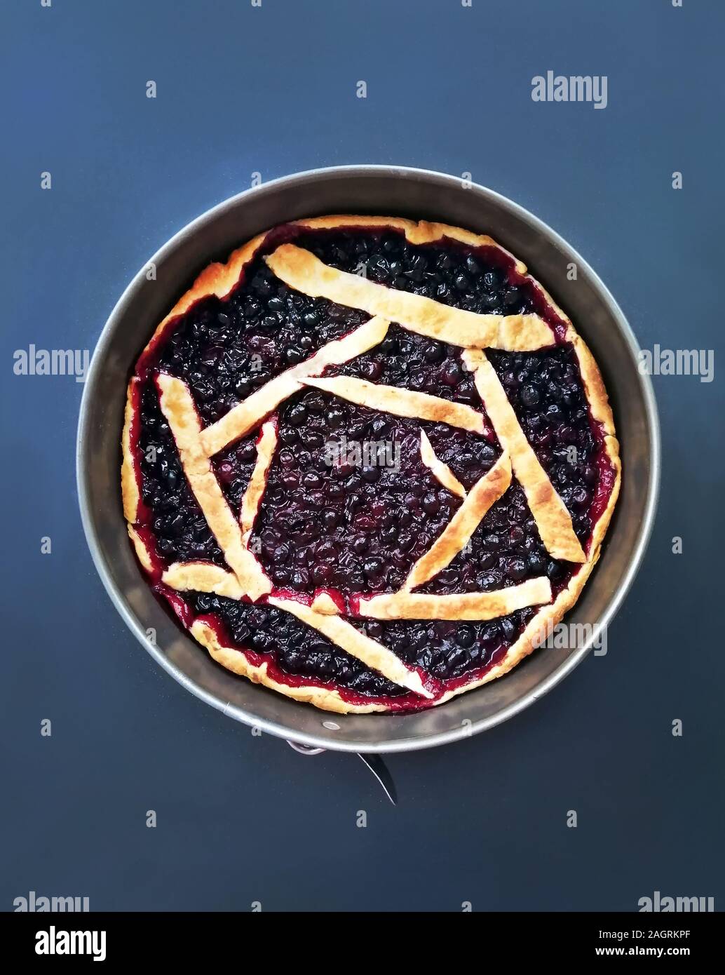 Round cake with black berries currant on a blue background, a recipe for sweet pastry from dough Stock Photo