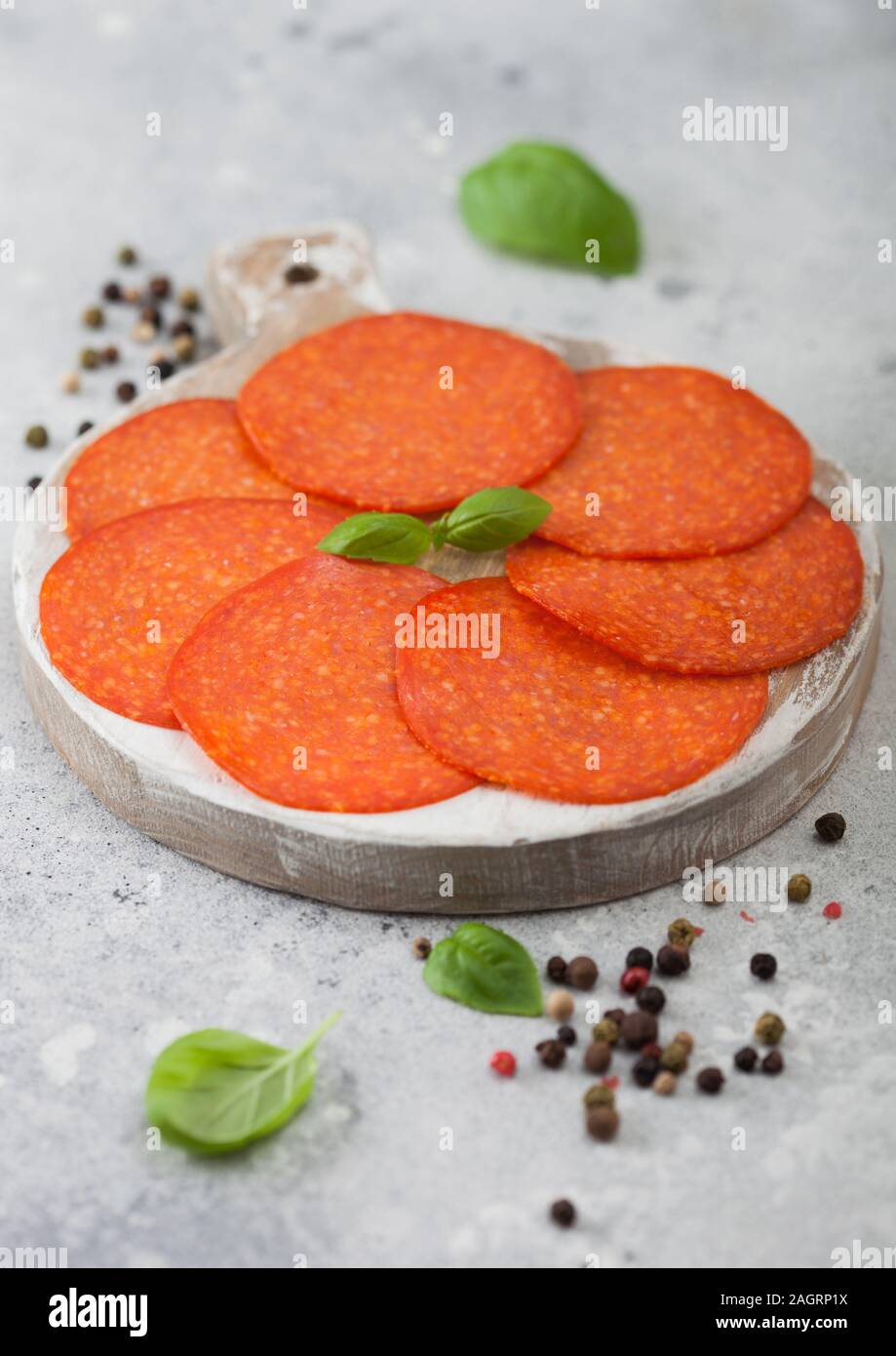 Spicy pepperoni salami with basil and pepper on wooden chopping board and light background Stock