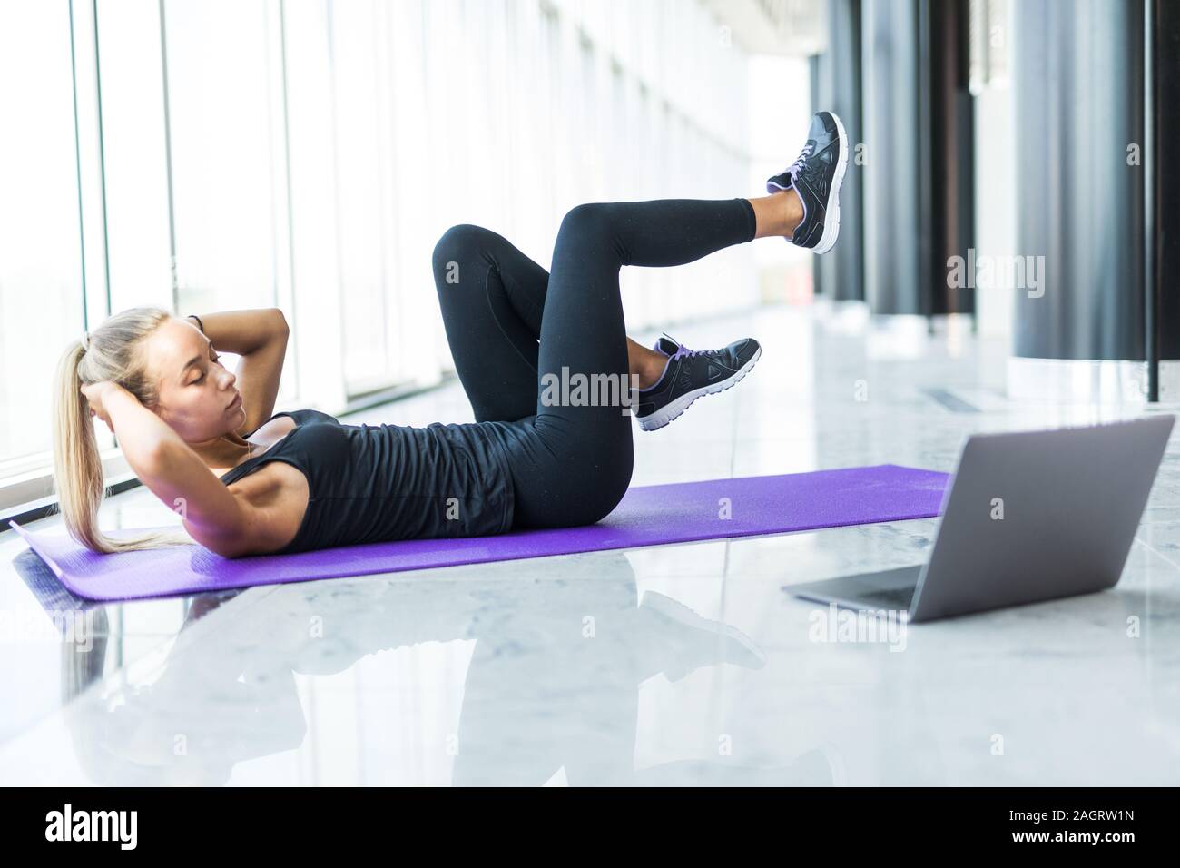 Girl makes yoga exercise online with laptop at gym Stock Photo