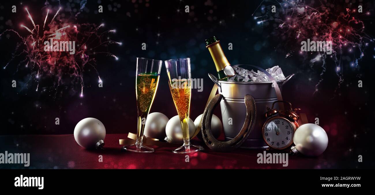 Festive New Year Party banner with champagne bottle and glasses, christmas decorations and red blue fireworks against a dark background in panoramic f Stock Photo