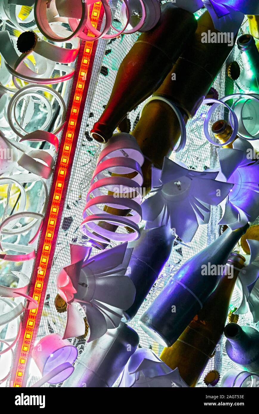 Close-up of a unusual Christmas decoration of recycled plastics and bottles combined with cold flower shaped lights and a diagonal red neon light Stock Photo