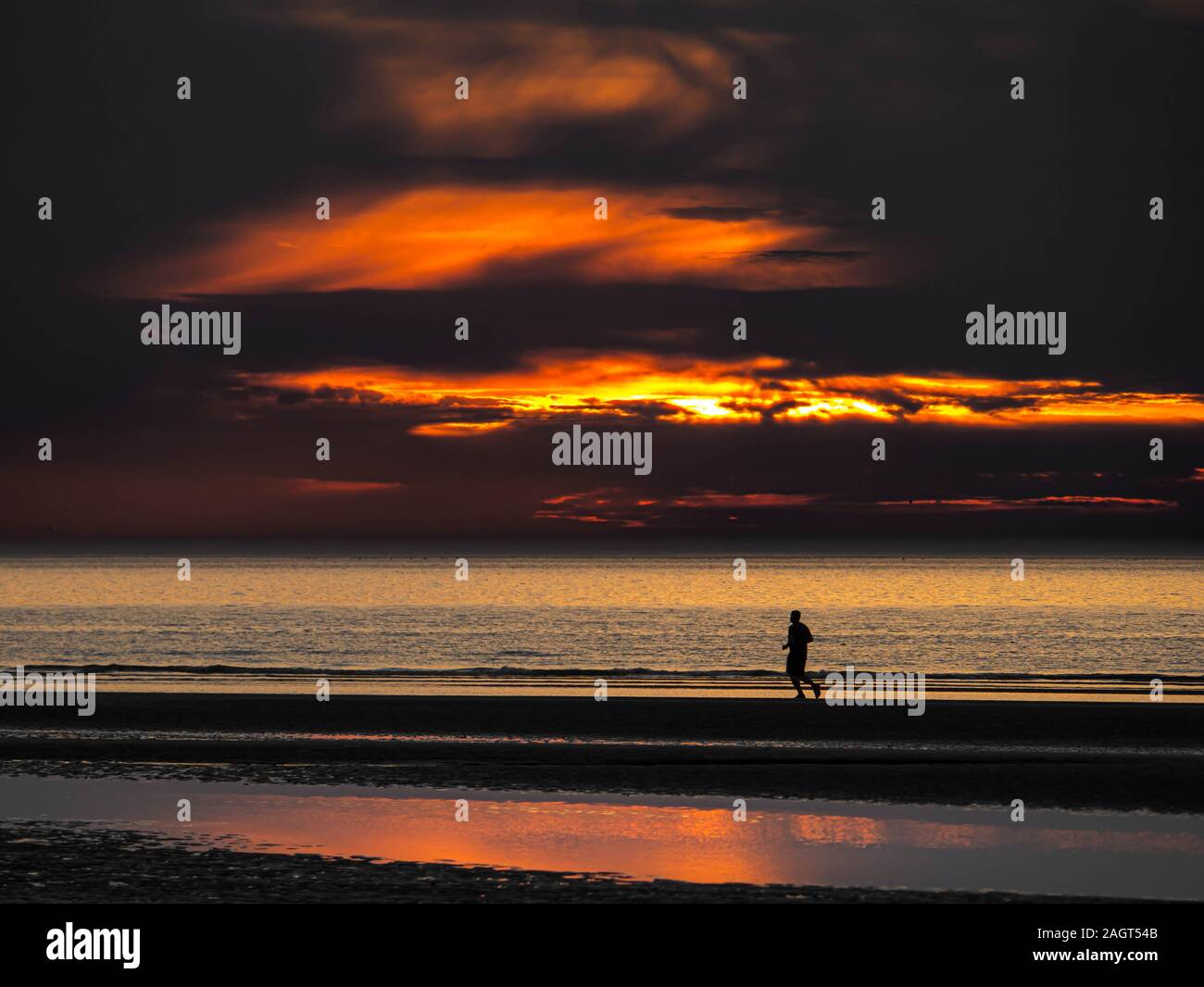 Single person running at an empty beach after colorful sunset Stock Photo