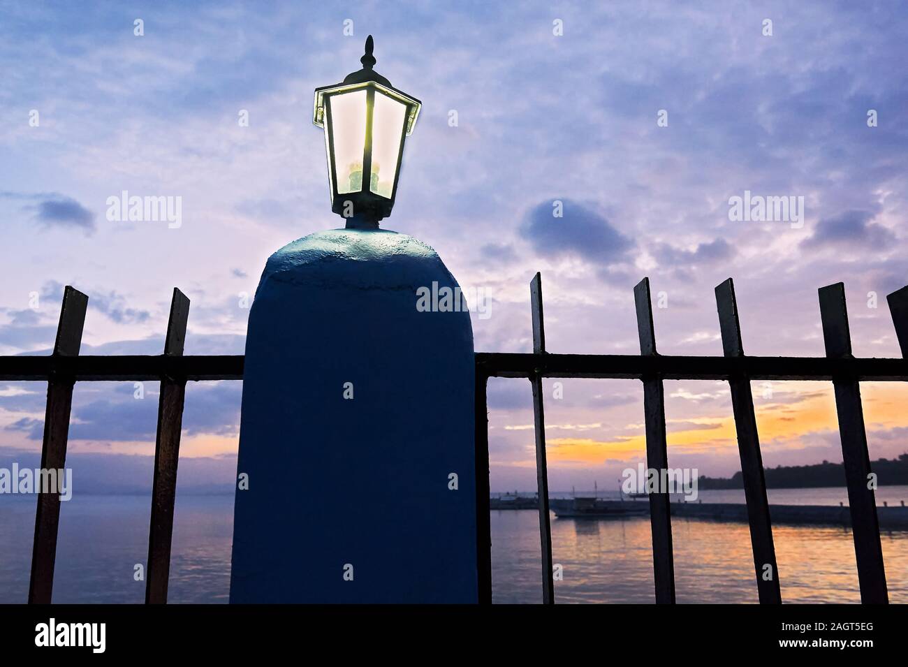 Colorful sunset with a metal fence and an illuminated fence light in the front, located at the Pier in San Vincente, Palawan Province, Philippines. Stock Photo