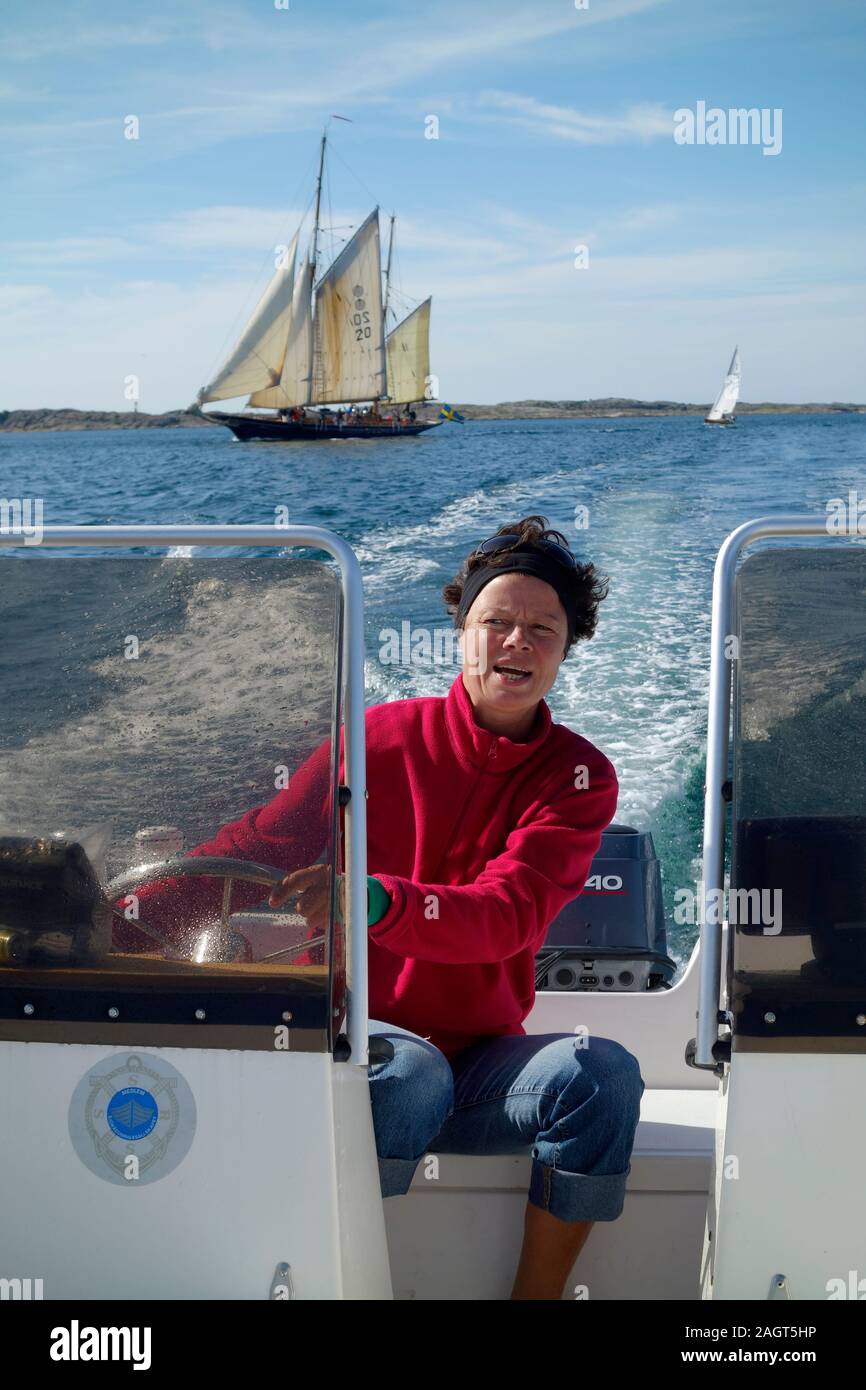 A woman steers a speed-boat on the calm sea. A schooner in background. Stock Photo