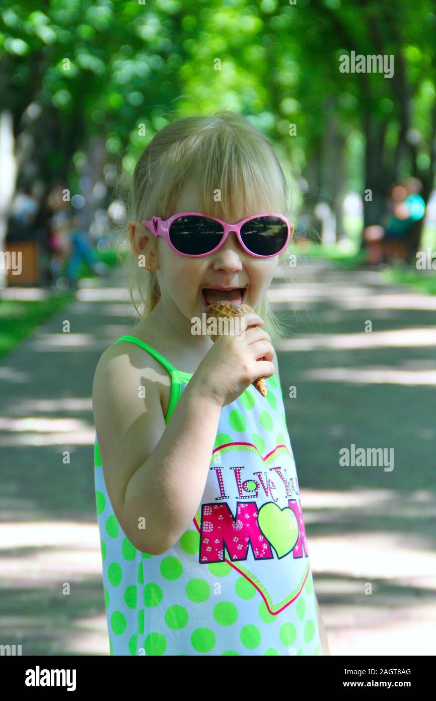 Little girl eating ice cream in city park. Baby girl in sunglasses eating icecream in summer park Stock Photo