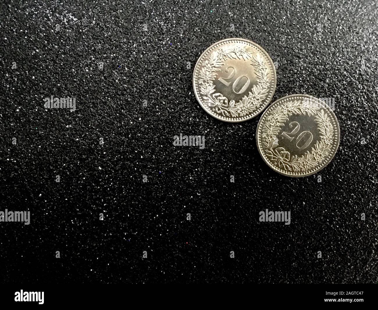 Two Swiss coins of twenty rappen on a black glittering background for new year 2020 with space for text. Stock Photo