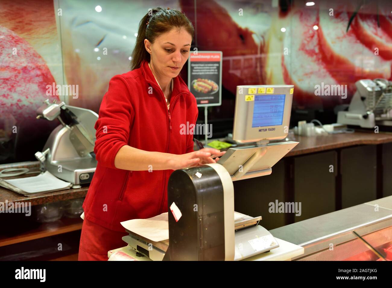 Woman weighing out meat at meat counter in Plodine supermarket, Bale, Croatia Stock Photo