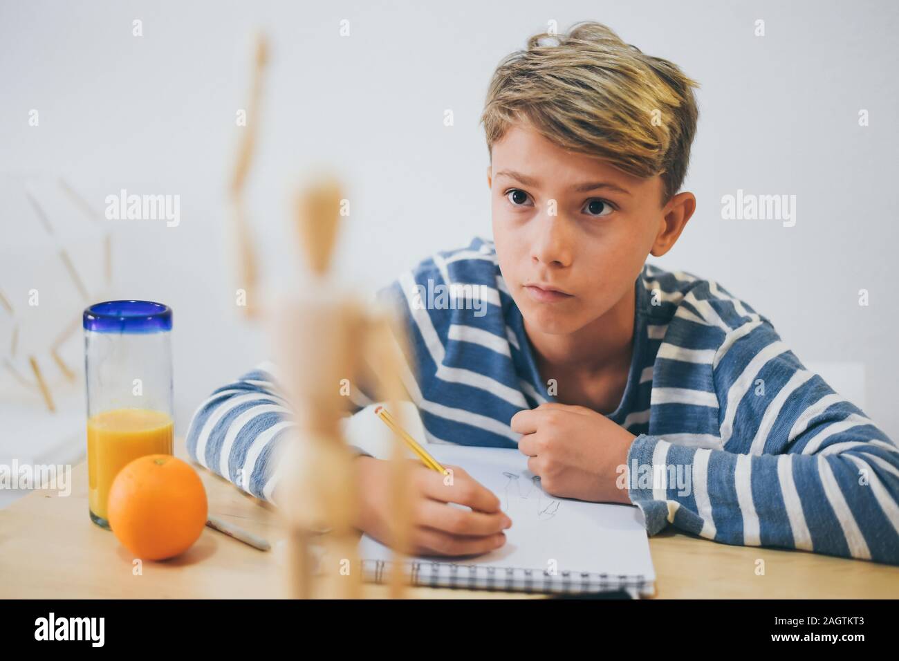 Student drawing with pencil a human figure be inspired by a wooden model. Boy copying a dummy