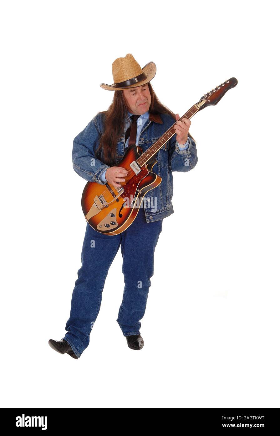 A handsome indigenous man in a jeans jacket, pants and a cowboy hat standing and playing the guitar, isolated for white background Stock Photo