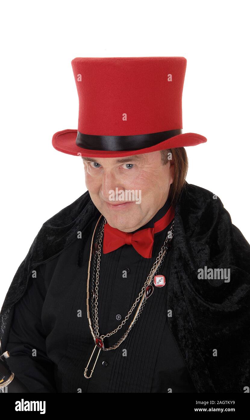A serious looking magician in a black outfit and a red hat looking into the camera with a bow tie and jewellery, isolated for white background Stock Photo
