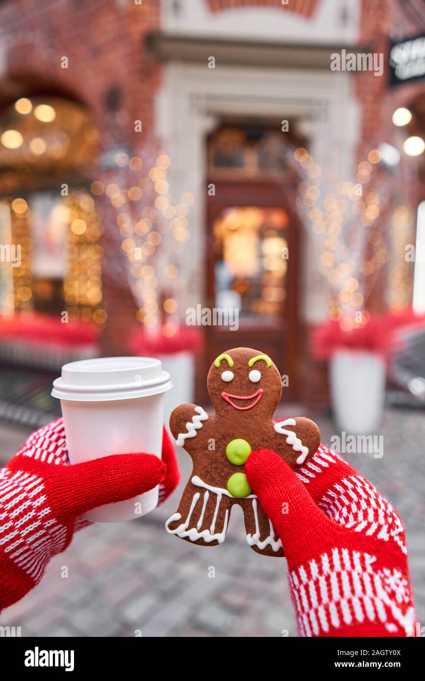 Hand in red mitten holding coffee cup and a smiling gingerbread man